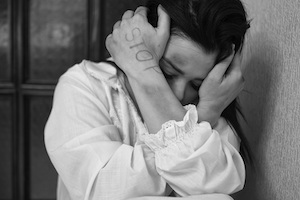 Los Angeles County Domestic Violence Defense Lawyer Woman Huddled Against a Wall with the Word “Stop” Written on Her Hand