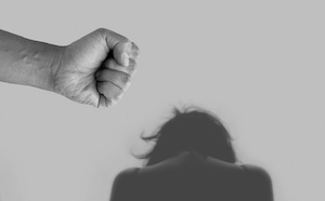 Los Angeles County Domestic Violence Defense Lawyer Close Up of a Fist with a Woman Huddled on the Floor in the Background