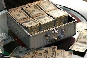 A Metal Suitcase Filled          with Money on a Table with Money Scattered Around