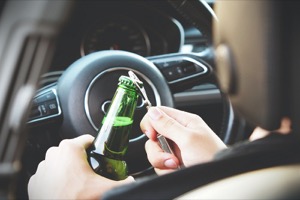 Person Sitting in a Driver Seat Holding a Bottle of Beer Holding a Bottle Opener to the Top.