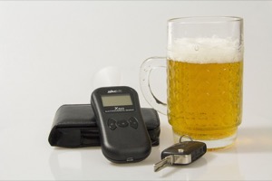 A Glass of Beer Sitting on a White Surface with a Breathalyzer and a Car Key Sitting Next to it.